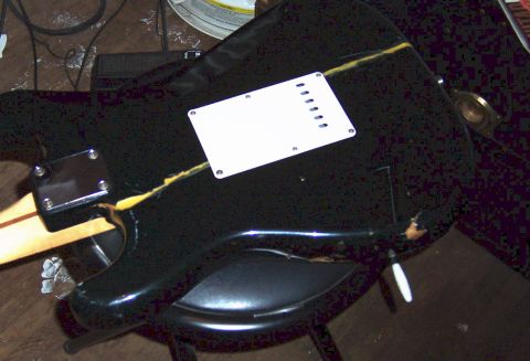 1975 Ford F-150 - The back of a black electric guitar body is shown, a white pickguard and visible damage to the binding.