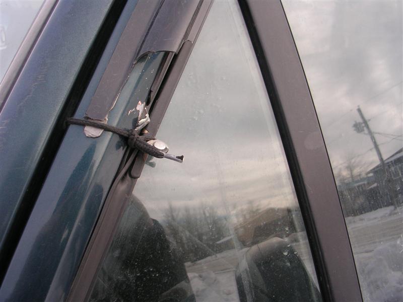 Close-up of black cord tied around broken window trim clip on a dark green vehicle's window frame