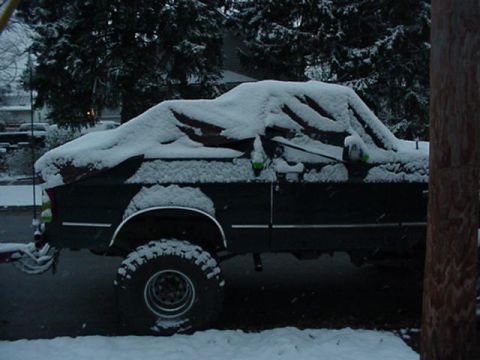 1992 Ford Bronco - Driver's-side profile of a dark, lifted full-size Ford SUV with the hardtop removed, buried under several inches of fresh snow in a residen…