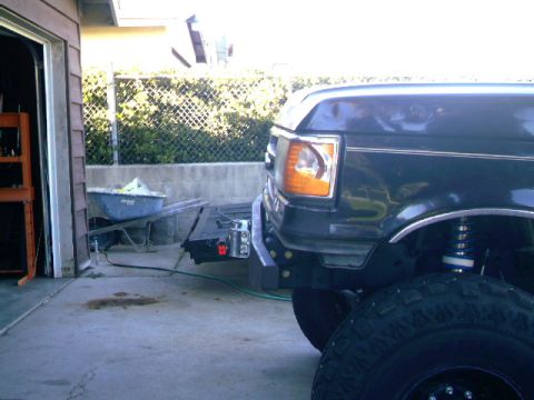 1989 Ford Bronco - The front bumper and fender of a dark-colored 1989 Ford Bronco are visible, with the headlight and wheel well in focus.