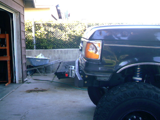 Front bumper and fender of a dark 1989 Ford Bronco, showing the headlight and wheel well