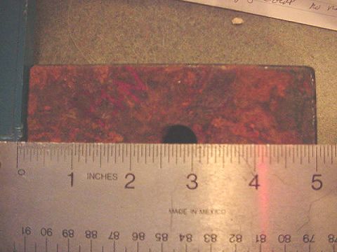 1992 Ford Bronco - A rusty rectangular steel block or bracket, roughly five inches wide with a single hole through its center, laid on a benchtop next to a st…