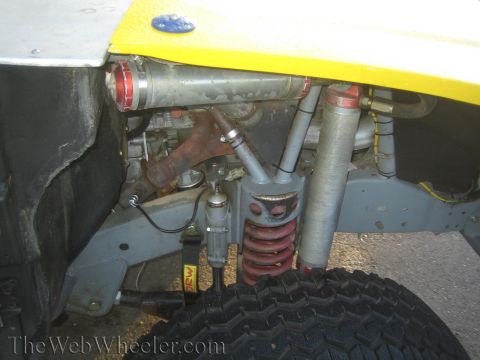 1990 Ford Bronco - Detail of an off-road vehicle's independent front suspension showing a red coilover spring and gas shock beneath yellow bodywork.