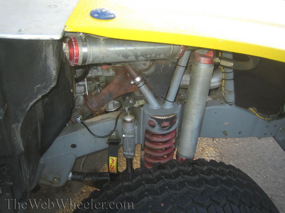 Close-up of vehicle front suspension with red coilover spring, smooth tire, and yellow bodywork