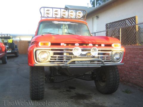 1990 Ford Bronco - Front view of a vintage orange Ford pickup with a roof-mounted light bar, four auxiliary lights, and a tubular brush guard.