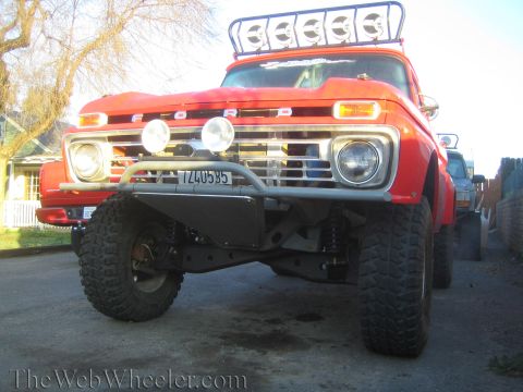 1990 Ford Bronco - Low front-angle view of a lifted orange Ford pickup with roof light bar, skid plate, and large off-road tires.