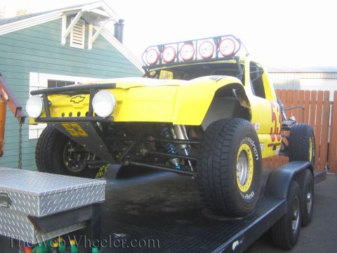 1990 Ford Bronco - yellow Chevrolet-bodied number 33 off-road race truck with roof light pods loaded on a flatbed trailer.