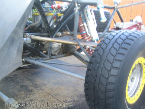 1990 Ford Bronco - Close view of a tube-chassis off-road truck's rear suspension with red coilovers, bypass shocks, and a smooth racing tire.