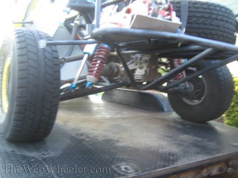 1990 Ford Bronco - Side view of an off-road truck's rear suspension on a trailer, showing red coilovers, trailing arms, and racing tires.