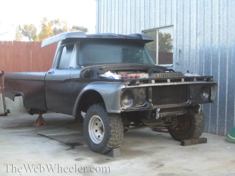 1990 Ford Bronco - vintage dark Ford pickup project on jack stands with the front end stripped and radiator exposed inside a metal shed.
