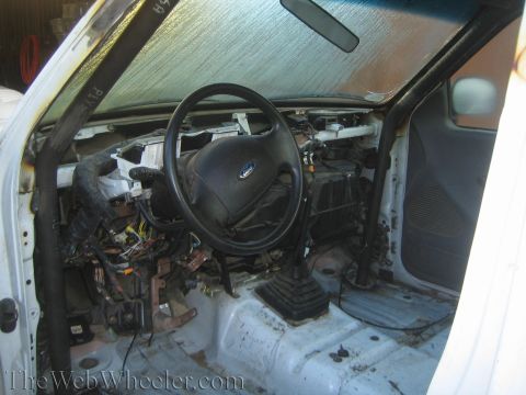 1990 Ford Bronco - Gutted interior of a white Ford truck showing the steering wheel with Ford emblem, pedals, and exposed dashboard wiring.