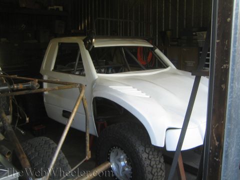 1990 Ford Bronco - Side view of a white fiberglass truck body and cab mounted on a tube chassis with oversized tire inside a storage shed.