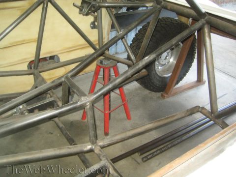 1990 Ford Bronco - bare welded tube-chassis frame under construction with a tire and red stool visible inside a workshop.