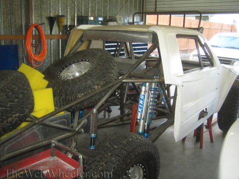 1990 Ford Bronco - off-road truck build with a white cab, blue King coilover shocks, and stacked spare tires inside a metal shed.