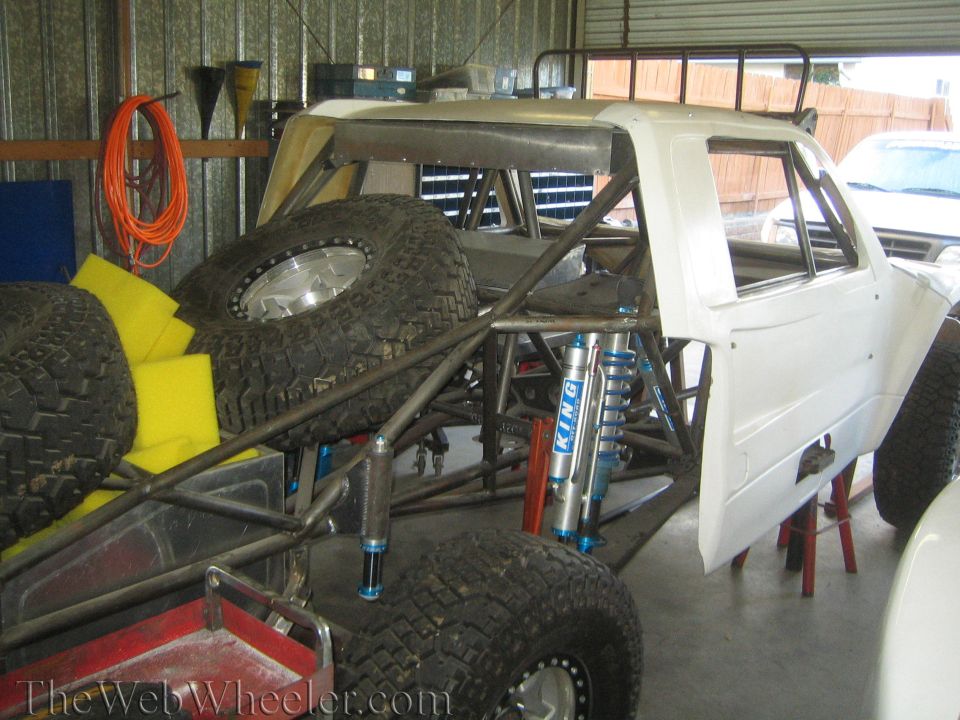Off-road truck build with white cab, King coilovers, and spare tires in a shed