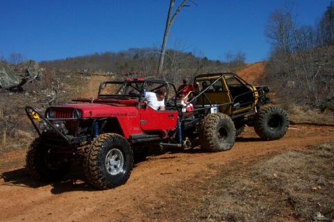 1990 Ford Bronco - Two custom off-road vehicles navigate a dusty trail under a clear blue sky.