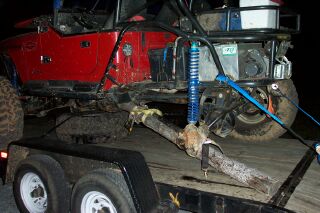 1990 Ford Bronco - A modified red Jeep Wrangler is loaded onto a trailer, highlighting its off-road capabilities and suspension system.