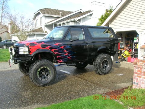 1996 Ford Bronco - This lifted Ford Bronco features custom flame graphics and is parked in a driveway.