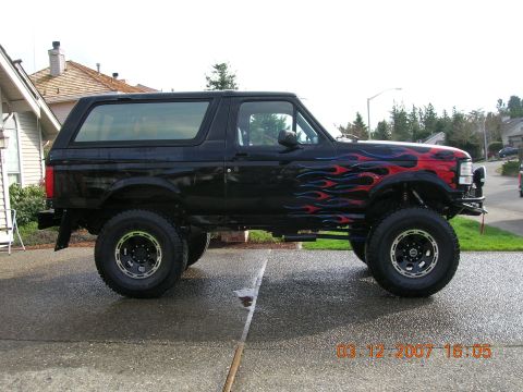 1996 Ford Bronco - A modified black Ford Bronco with flame decals is shown from the side on a wet day.