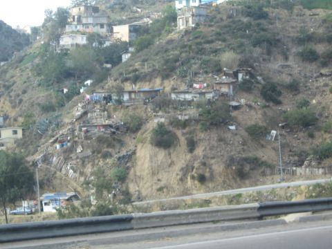 1990 Ford Bronco - hillside crowded with makeshift shacks and small homes rises beyond a metal highway guardrail.
