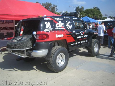 1990 Ford Bronco - Rear view of a black and red number 30 Donahoe Racing Toyota FJ Cruiser off-road truck with a spare tire on a front rack.