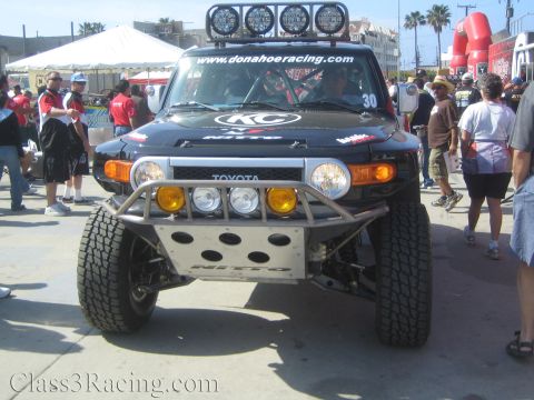 1990 Ford Bronco - Head-on view of a black number 30 Donahoe Racing Toyota FJ Cruiser off-road truck amid a crowd of spectators.