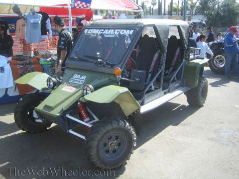 1990 Ford Bronco - green long-wheelbase tube-frame off-road buggy lettered "10MCAR.com" and "Baja Proven" parked at a crowded event lot.