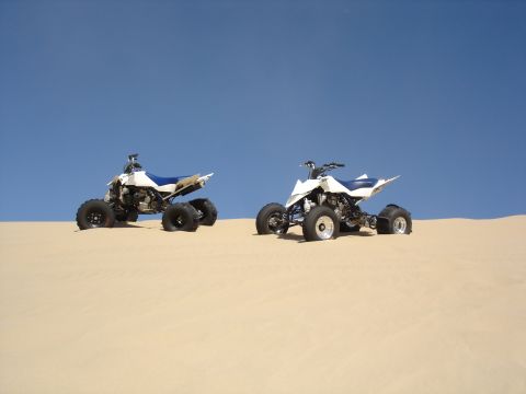 1996 Ford Bronco - Two ATVs are parked on a sandy dune with a clear blue sky above.