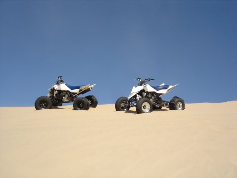 1996 Ford Bronco - Two ATVs sit on a sandy dune with a bright blue sky overhead.
