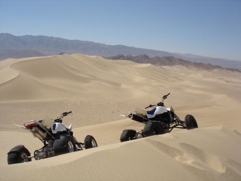 1996 Ford Bronco - Two ATVs are parked in the sand dunes under a clear blue sky with mountains in the distance.