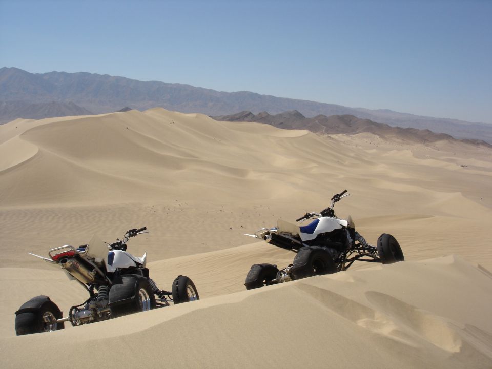 Two ATVs in sand dunes with mountains in background