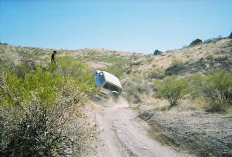 1996 Ford Bronco - SUV tips over on a steep, dusty trail in a dry, hilly landscape.