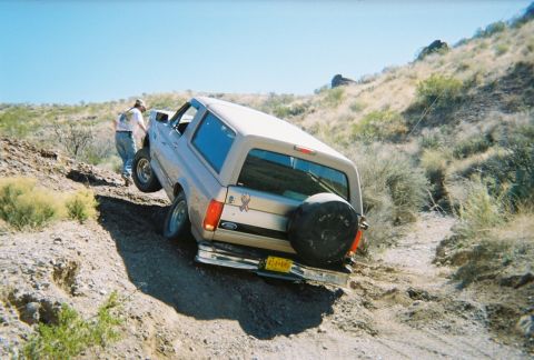 1996 Ford Bronco - A tan Ford Bronco navigates a steep, off-road trail with a person standing nearby.