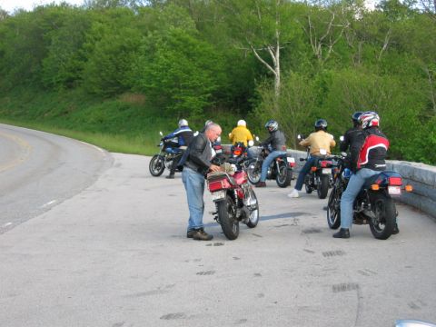 1985 Ford LTD Crown Victoria - A group of motorcyclists have pulled over on a scenic road, with several bikes parked and riders gathered.