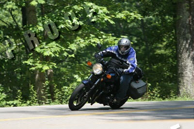 1985 Ford LTD Crown Victoria - A motorcyclist rides a dark blue motorcycle with saddlebags on a tree-lined road.