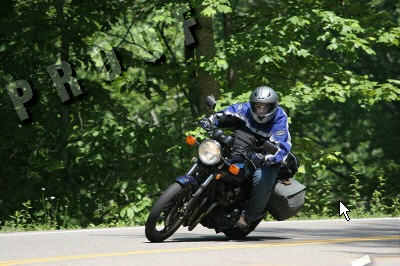 1985 Ford LTD Crown Victoria - Rider on a motorcycle navigates a curve on a tree-lined road.