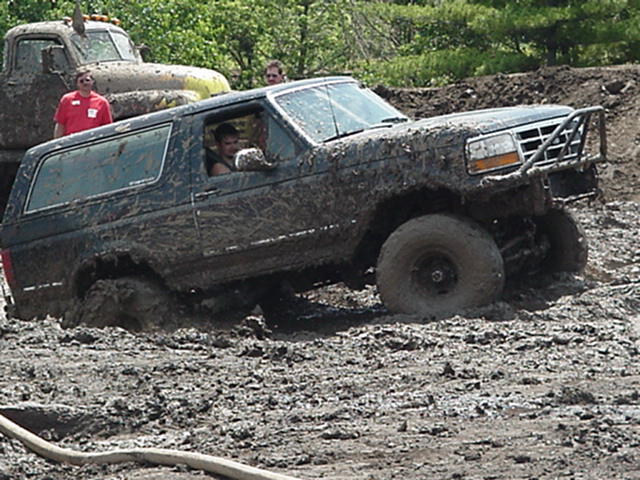 Driver in a mud-coated Bronco sunk to the doors in a mud bog, spectators watching