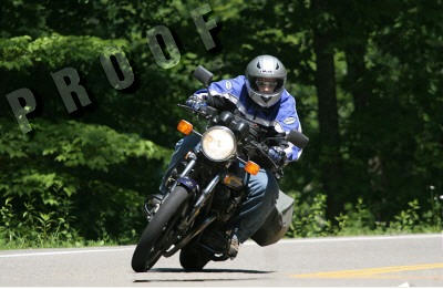 1985 Ford LTD Crown Victoria - A motorcycle rider navigates a curve on a tree-lined road.
