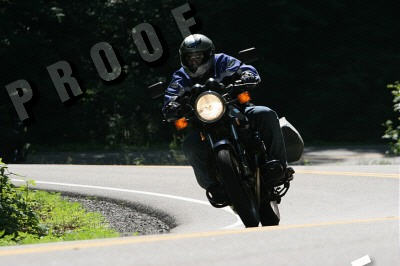 1985 Ford LTD Crown Victoria - Rider on a motorcycle navigates a sharp turn on a tree-lined road.