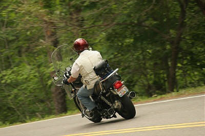 1985 Ford LTD Crown Victoria - A rider on a motorcycle navigates a curve on a tree-lined road.