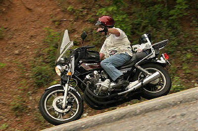1985 Ford LTD Crown Victoria - A rider on a motorcycle navigates an uphill road surrounded by greenery.