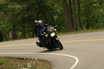 1985 Ford LTD Crown Victoria - Motorcycle riders navigate a sharp turn on a scenic road surrounded by trees.