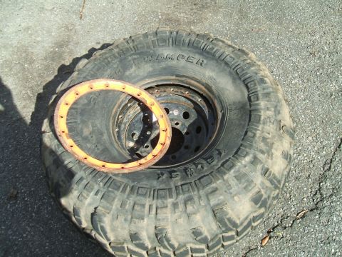1995 Ford Bronco - A tire and beadlock ring are shown on a paved surface. The tire has aggressive tread and visible text.