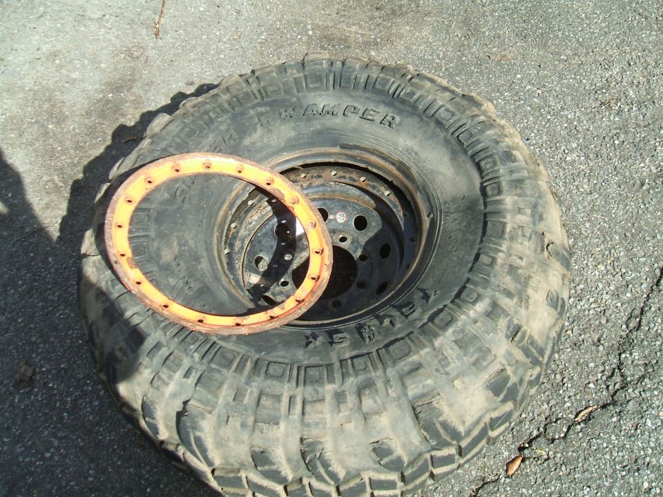 Off-road tire with a beadlock ring sitting on the tread. Tire has 'SWAMPER' text