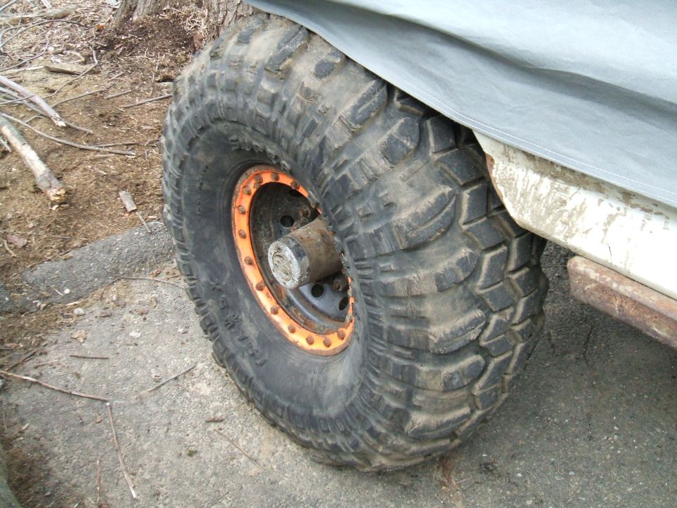 Off-road tire with orange beadlock on a vehicle covered by a gray tarp