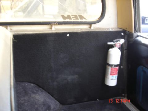 1979 Ford Bronco - The interior of a vehicle shows a black panel with a fire extinguisher attached.