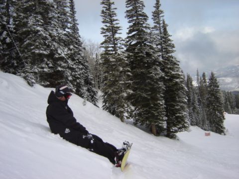 1992 Ford Bronco - A snowboarder takes a break on a snow-covered mountain, surrounded by tall pine trees.