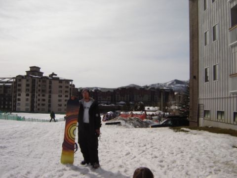 1992 Ford Bronco - A snowboarder stands in the snow with a snowboard, while buildings and mountains are visible in the distance.