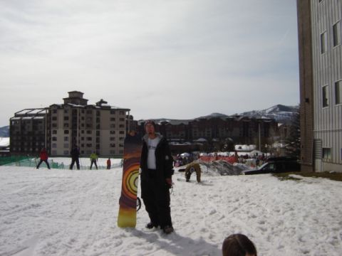 1992 Ford Bronco - A snowboarder stands in a snowy resort area with large buildings and mountains in the background.