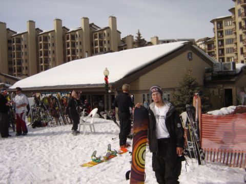 1992 Ford Bronco - A snowboarder stands in the snow outside a ski lodge, surrounded by winter sports equipment.